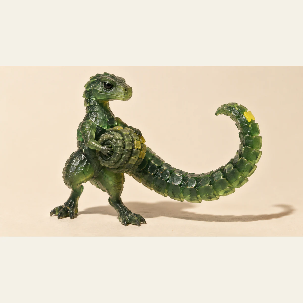 A translucent green resin dinosaur holds a tightly packed, rounded coil beside its long, sharply scaled tail. Yellow accents punctuate the resin, with a hard shadow across the ivory background.