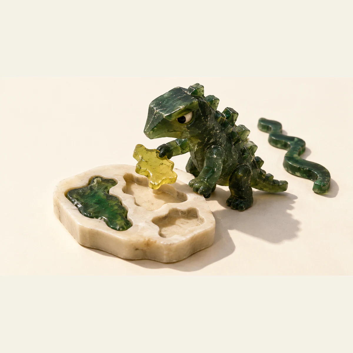 A skeptical green resin dinosaur holds a yellow puzzle piece above an ivory tray with one fitted green piece and empty cavities. A separate winding green strand lies behind it, all casting shadows on warm ivory.