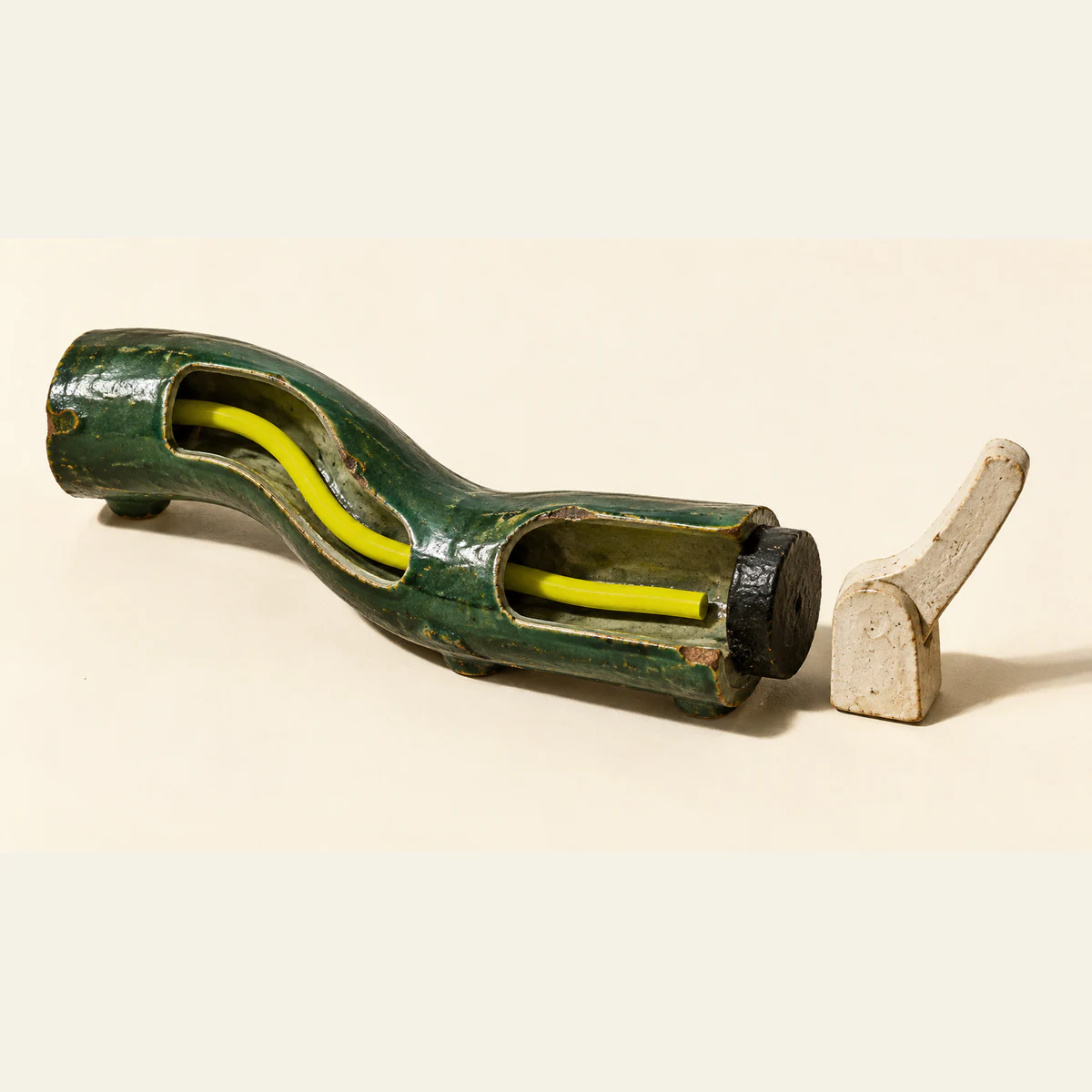 A chipped forest-green ceramic conduit exposes a yellow trace through two openings. The trace ends before a black stopper, with a separate raised ivory lever beyond it, on a warm ivory background.