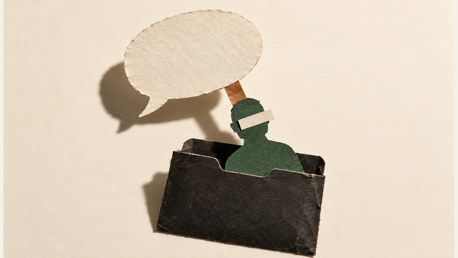 A blank paper speech bubble connects by a copper-colored tab to a green human silhouette emerging from a worn black folder. An ivory strip covers its eyes; hard shadows fall across the ivory background.