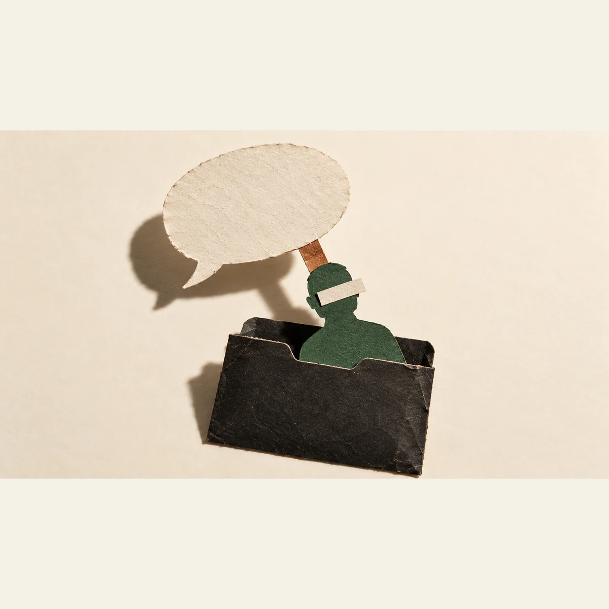 A blank paper speech bubble connects by a copper-colored tab to a green human silhouette emerging from a worn black folder. An ivory strip covers its eyes; hard shadows fall across the ivory background.
